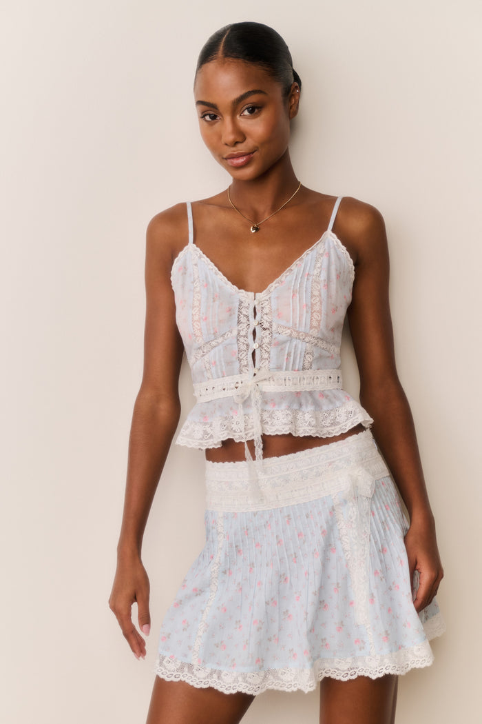 Woman wearing a light blue floral skirt and top against a beige background