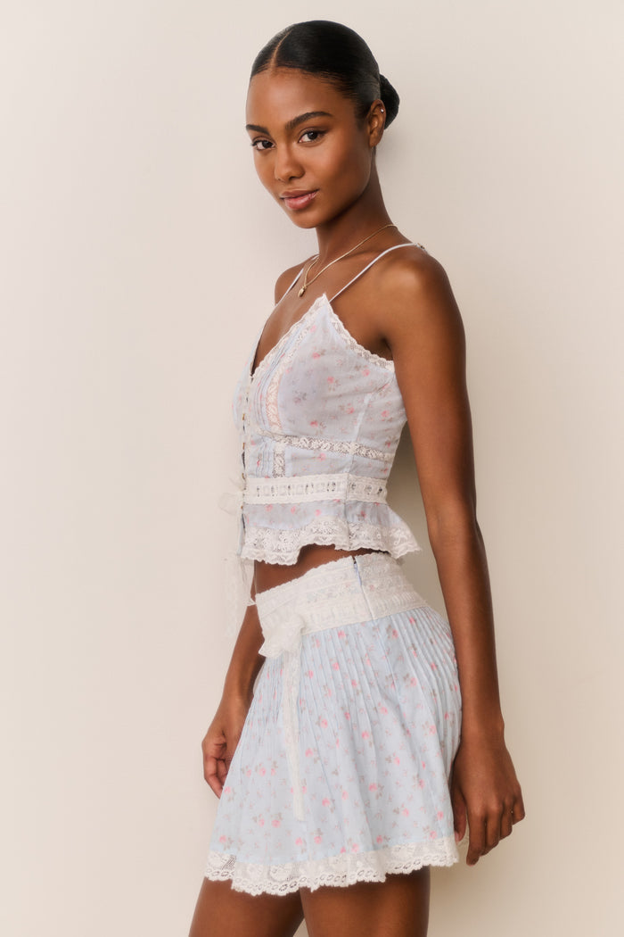 Woman wearing a light blue floral skirt and top against a beige background