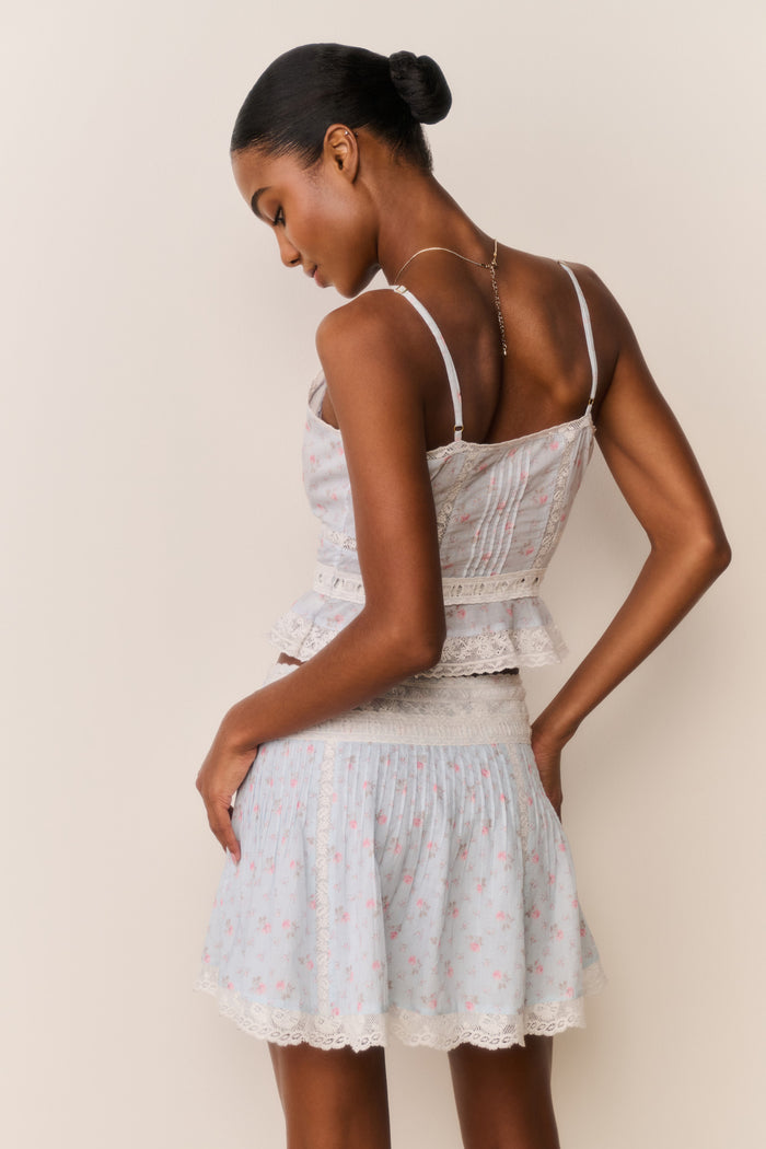 Woman wearing a light blue floral skirt and top against a beige background