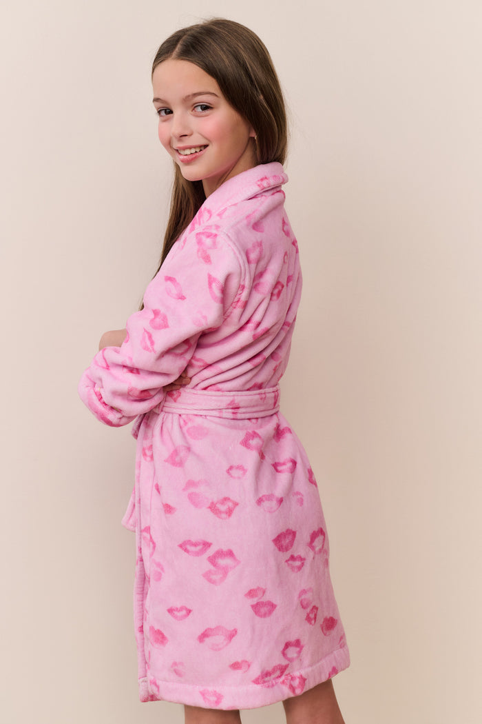 Young girl wearing a pink robe with lip prints on a beige background