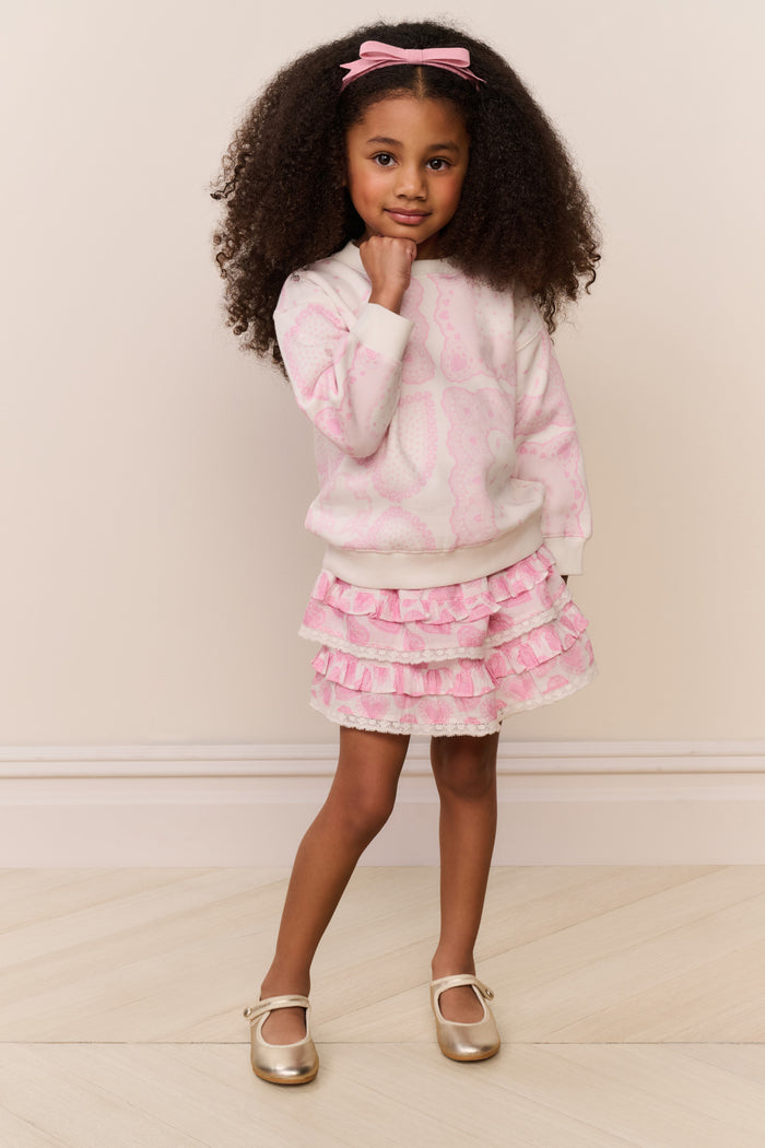 Young girl in a pink and white outfit with ruffled skirt standing against a plain background