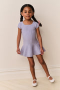 Young girl wearing a light blue dress with square neckline standing against a plain background
