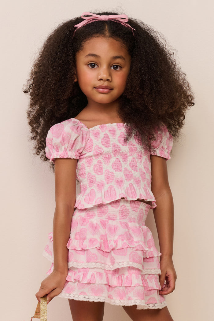 Young girl wearing a pink heart set with ruffles against a plain background