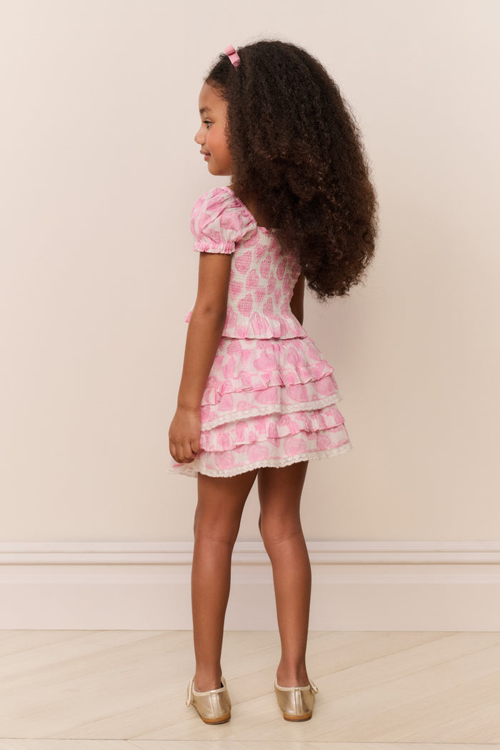 Young girl wearing a pink floral dress standing against a plain background