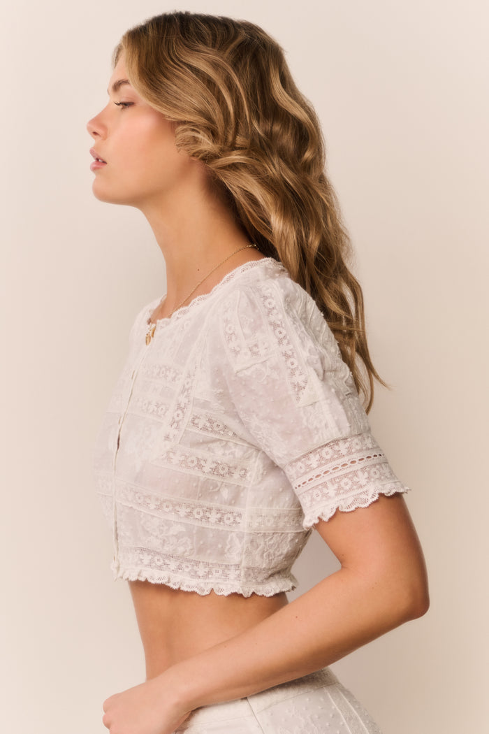 Woman wearing a white lace top against a plain background