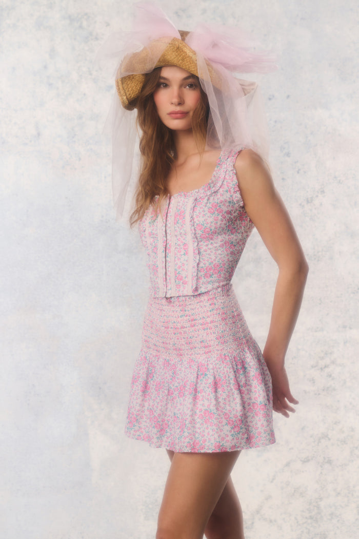 Woman wearing a floral dress and matching hat with a veil against a light background