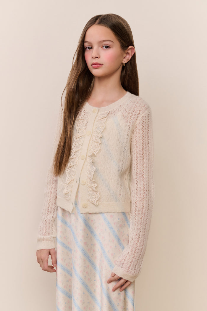 Young girl wearing a cream-colored sweater with rufflees against a beige background